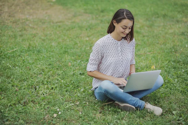 Jeune femme avec ordinateur portable assis sur l'herbe verte — Photo