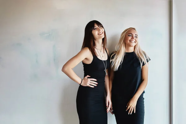 Zwei hübsche Frauen in einem schwarzen Kleid drinnen — Stockfoto