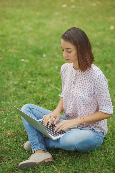 Giovane donna con computer portatile seduto su erba verde — Foto Stock