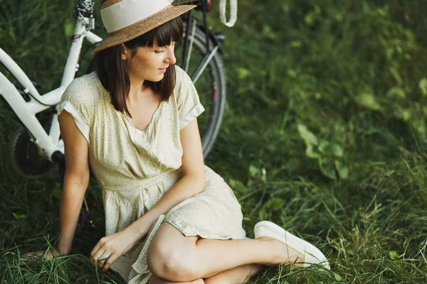 Außenporträt der attraktiven jungen Brünette mit Hut auf einem Fahrrad. — Stockfoto