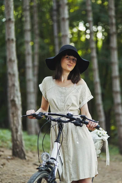 Venkovní portrét atraktivní mladá brunetka v klobouku na kole. — Stock fotografie