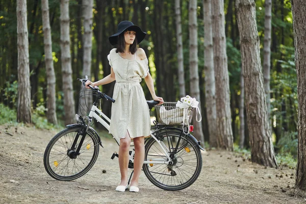 Retrato ao ar livre de jovem morena atraente em um chapéu em uma bicicleta . — Fotografia de Stock