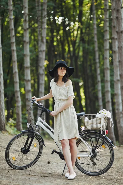 Retrato al aire libre de la atractiva joven morena en un sombrero en una bicicleta . —  Fotos de Stock