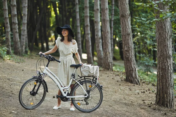 Außenporträt der attraktiven jungen Brünette mit Hut auf einem Fahrrad. — Stockfoto