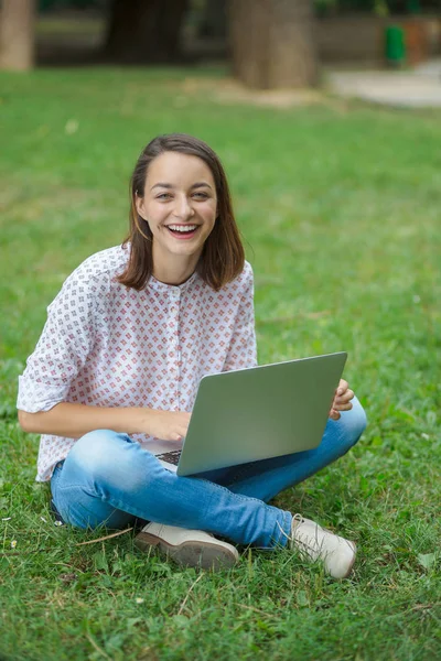 有笔记本电脑的年轻女人坐在绿草上 — 图库照片