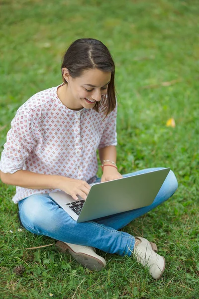 Young woman with laptop sitting on green grass — Stock Photo, Image