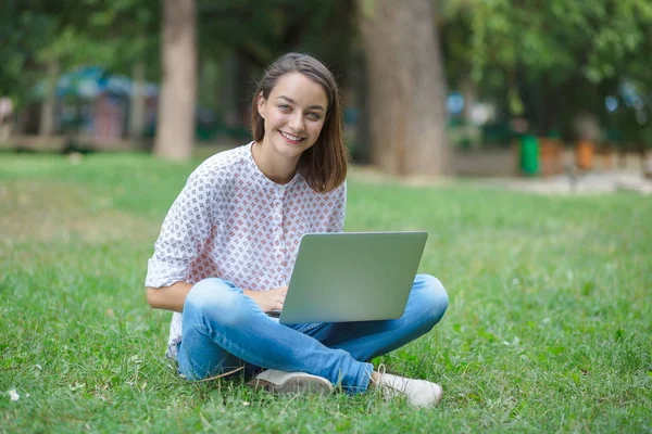 Giovane donna con computer portatile seduto su erba verde — Foto Stock