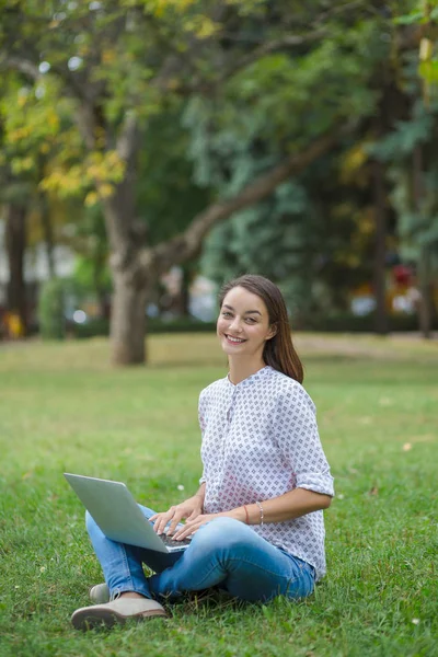 Молодая женщина с ноутбуком сидит на зеленой траве — стоковое фото