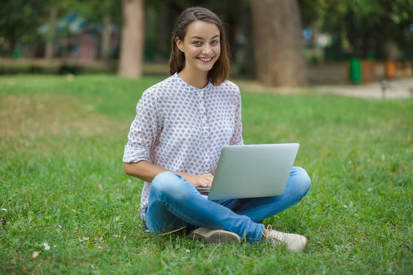 Junge Frau mit Laptop sitzt auf grünem Gras — Stockfoto