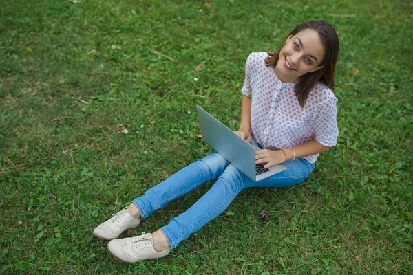 Junge Frau mit Laptop sitzt auf grünem Gras — Stockfoto