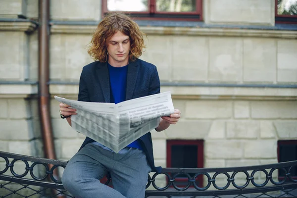 Jovem homem avermelhado ler jornal perto de edifício de estilo antigo — Fotografia de Stock