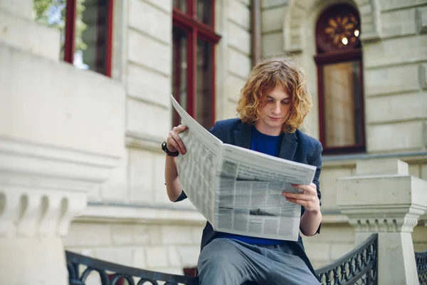 Młody człowiek czerwonawy, czytanie gazety w pobliżu centrum — Zdjęcie stockowe