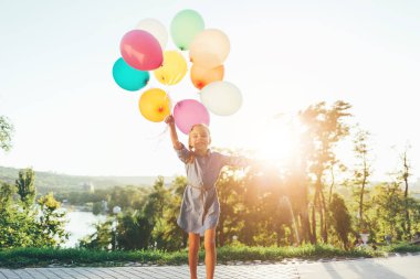 Mutlu kız renkli balonlar oynarken şehir parkında tutarak bir