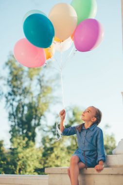 Renkli balonlar otururken onlara bakarak tutan kız