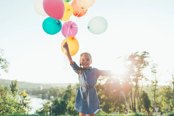 Chica feliz sosteniendo globos de colores en el parque de la ciudad, jugando un — Foto de Stock