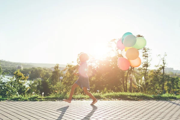 Menina bonito segurando balões coloridos no parque da cidade, jogando, r — Fotografia de Stock