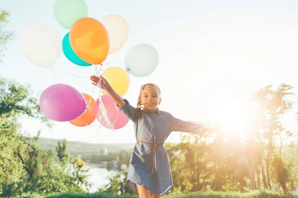 Chica feliz sosteniendo globos de colores en el parque de la ciudad, jugando un — Foto de Stock