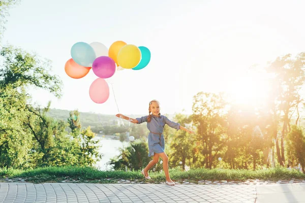 Roztomilá dívka drží barevné balónky v městském parku hraje — Stock fotografie