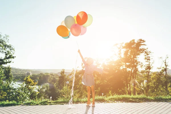 Flickan håller färgglada ballonger sträcker sig mot himlen — Stockfoto