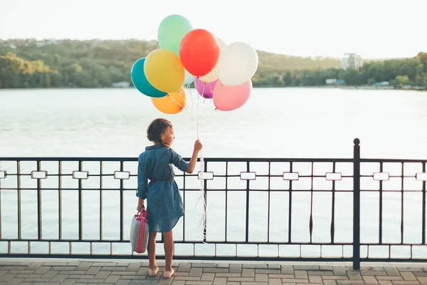 Wesoła dziewczyna gospodarstwa kolorowe balony i dziecinna walizka wa — Zdjęcie stockowe