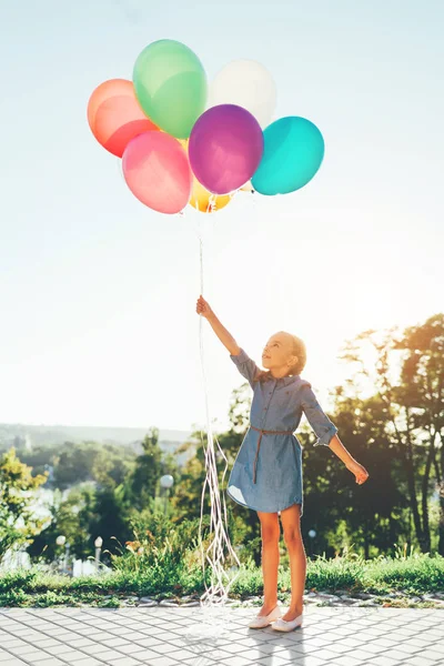 Chica sosteniendo globos de colores que se extienden hasta el cielo y el sueño — Foto de Stock