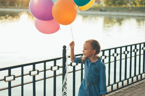 性格开朗的女孩，抱着五颜六色的气球带着孩子气的手提箱洼 — 图库照片