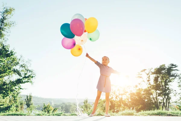 Усміхнена мила дівчина тримає барвисті кульки в міському парку — стокове фото