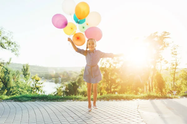 Щаслива дівчина тримає барвисті повітряні кулі в міському парку, граючи — стокове фото