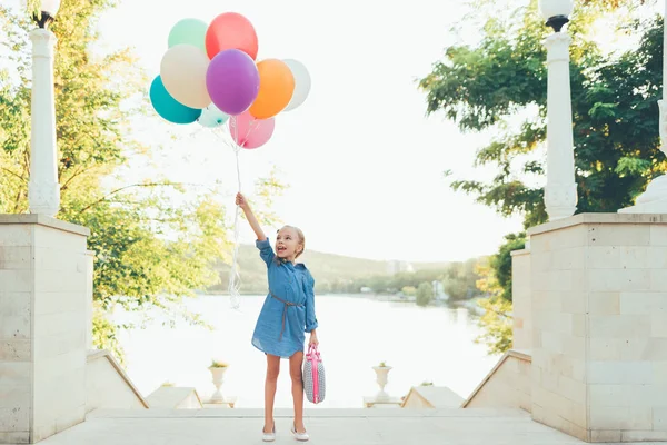 Glad tjej håller färgglada ballonger och barnslig resväska — Stockfoto