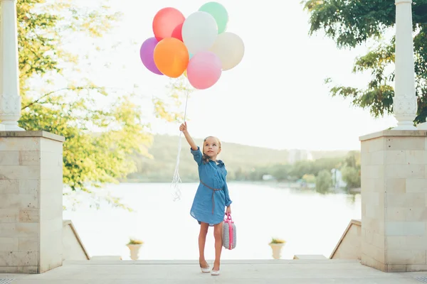 Glad tjej håller färgglada ballonger och barnslig resväska — Stockfoto