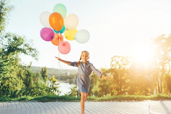 Mutlu kız renkli balonlar oynarken şehir parkında tutarak bir