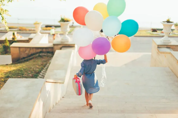 Девушка бежит по лестнице с цветными воздушными шарами и детьми — стоковое фото