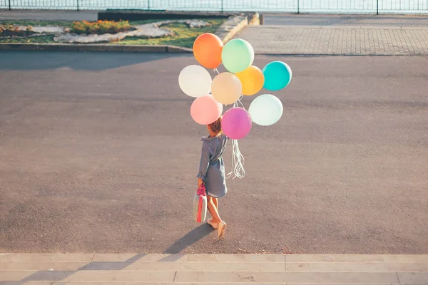 Веселая девушка с красочными воздушными шарами и детским чемоданом ва — стоковое фото