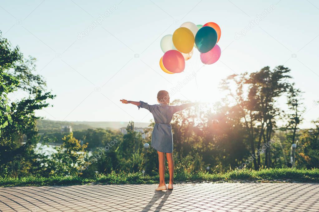 Cute girl holding colorful balloons in the city park spreding ar