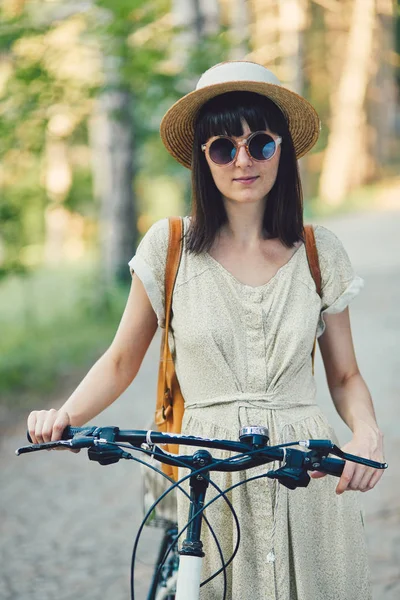 Außenporträt der attraktiven jungen Brünette mit Hut auf einem Fahrrad. — Stockfoto