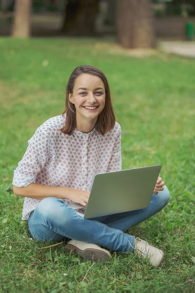 Young woman with laptop sitting on green grass — Stock Photo, Image