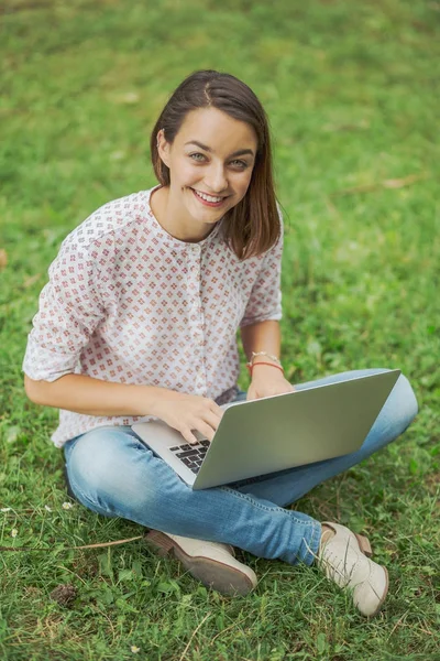 Young woman with laptop sitting on green grass — Stock Photo, Image