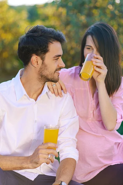 Casal feliz beber suco de laranja no parque olhando para cada o — Fotografia de Stock