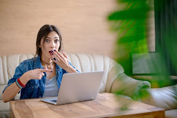 Mujer joven sorprendida mostrando con el dedo a la pantalla del ordenador portátil . — Foto de Stock