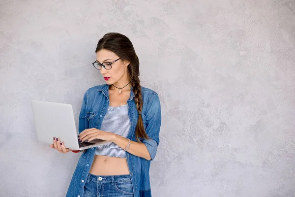 Donna in occhiali in piedi focalizzata sul computer portatile — Foto Stock