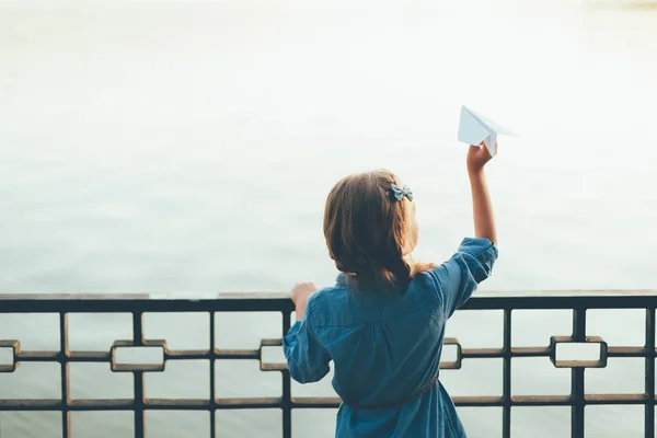 Девушка с игрушечной бумагой самолет глядя на озеро — стоковое фото