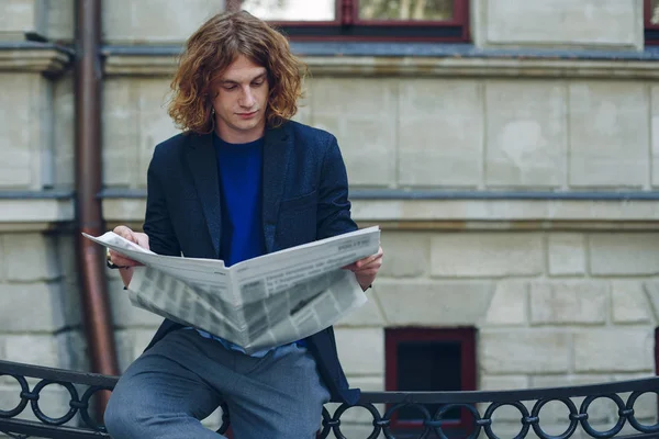 Vöröses fiatalember olvasó újság régi stílusú épület közelében — Stock Fotó