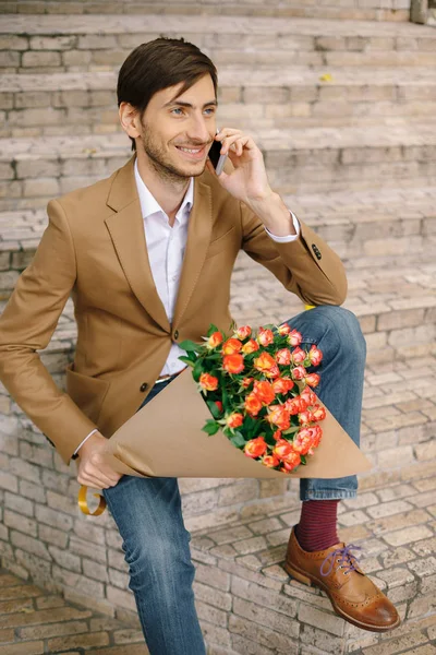 Hombre guapo sosteniendo ramo de rosas hablando feliz por teléfono —  Fotos de Stock