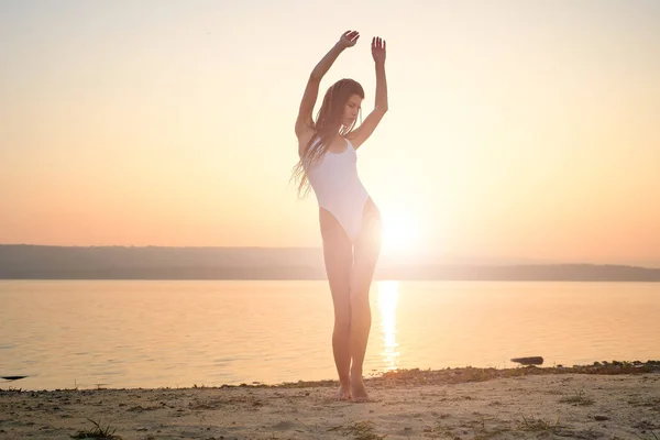 Mujer joven en traje de baño de cuerdas se para en la playa al amanecer — Foto de Stock