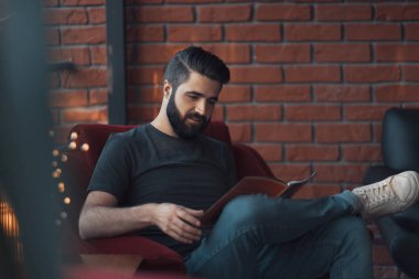 Portrait handsome bearded man wearing casual clothing, sitting in red chair modern loft studio