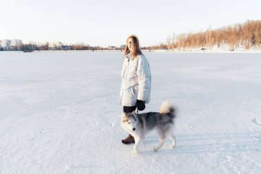 Mutlu genç kız kış parkında Sibirya köpeğiyle oynuyor.