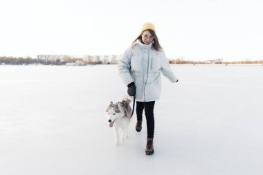 Mutlu genç kız kış parkında Sibirya köpeğiyle oynuyor.