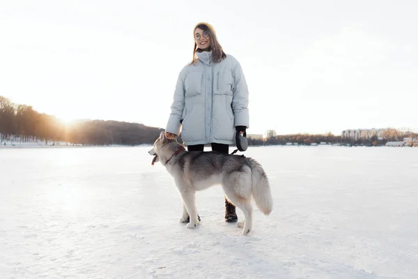 Szczęśliwa młoda dziewczyna bawi się z syberyjskim husky dog w parku zimowym — Zdjęcie stockowe