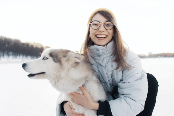 Szczęśliwa młoda dziewczyna bawi się z syberyjskim husky dog w parku zimowym — Zdjęcie stockowe