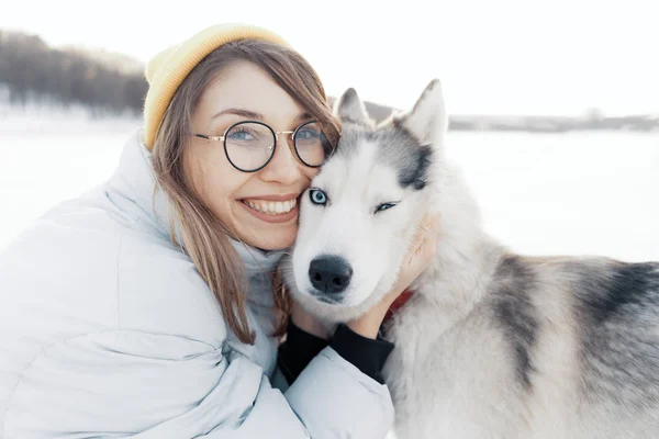 Szczęśliwa młoda dziewczyna bawi się z syberyjskim husky dog w parku zimowym — Zdjęcie stockowe